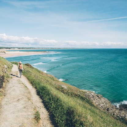 Randonneuse, GR223, herbe, chemin sur falaise longeant la mer bleue, ciel bleu, plage sable au loin - © Maxime Coquard pour les Best Jobers - Attitude Manche