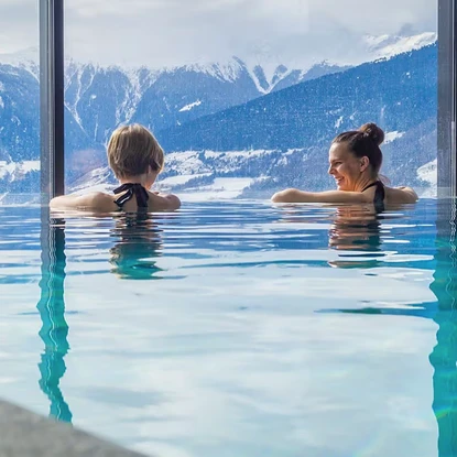 Deux femmes se relaxant dans une piscine chauffée avec une vue panoramique sur des montagnes enneigées.