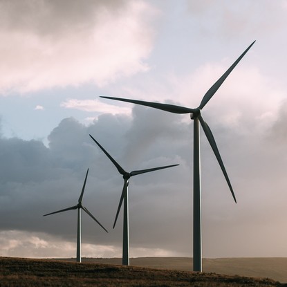Éoliennes sur une colline herbeuse sous un ciel nuageux.
