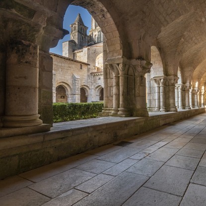 Vue en profondeur sur le cloître de l’abbaye qui est pavé au sol et possédant de somptueuses colonnes sculptées et voûtes au plafond