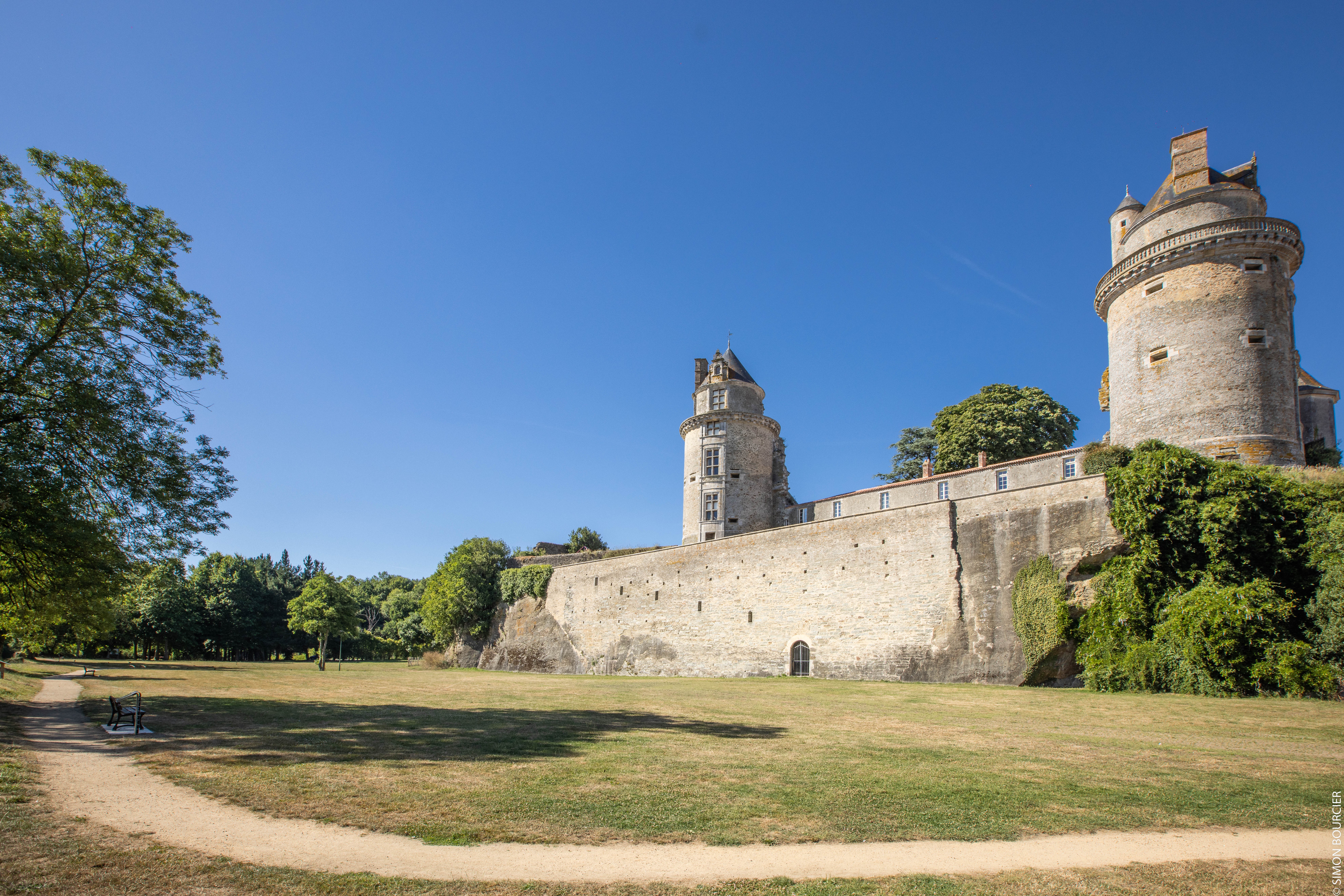 Parc avec du gazon vert devant les deux tours du château d’Apremont sous un ciel bleu