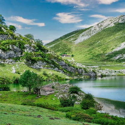 Lac entouré de montagnes verdoyantes et d'un chalet en arrière-plan sous un ciel bleu.