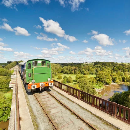 Train de la Vendée passant sur un pont au dessus d’une rivière dans une campagne  verdoyante