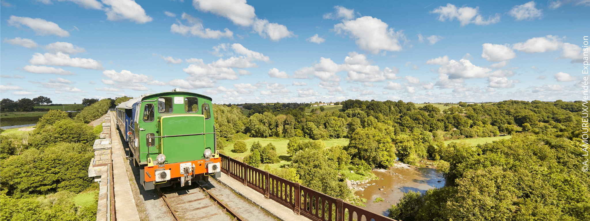 Train de la Vendée passant sur un pont au dessus d’une rivière dans une campagne  verdoyante
