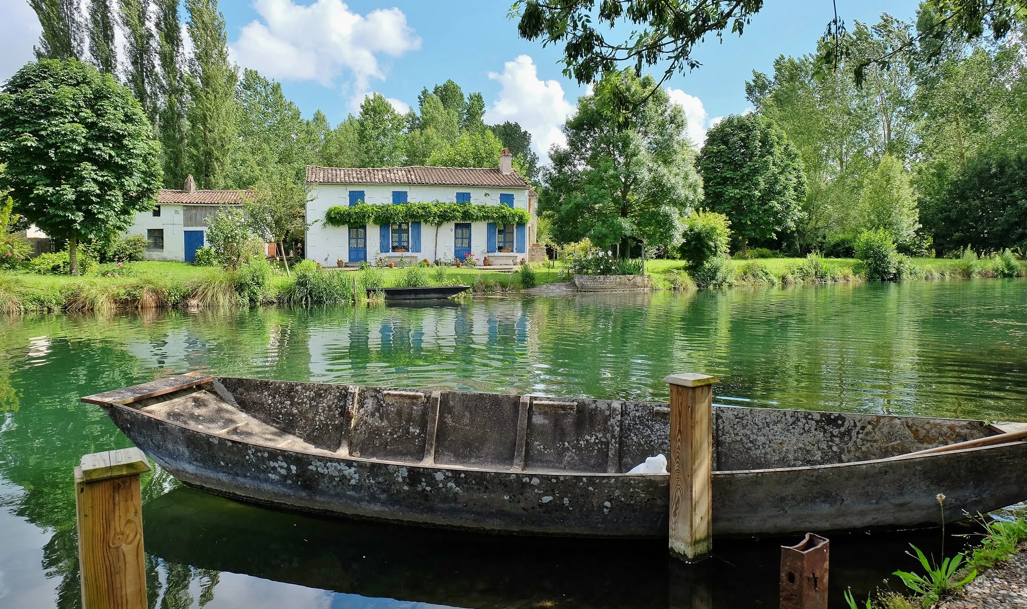 Barque amarrée sur le marais aussi appelé Venise Verte devant une maison maraîchine entourée de verdure.