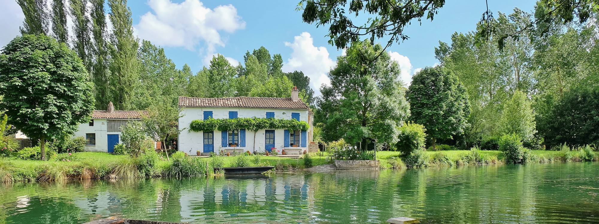 Barque amarrée sur le marais aussi appelé Venise Verte devant une maison maraîchine entourée de verdure.