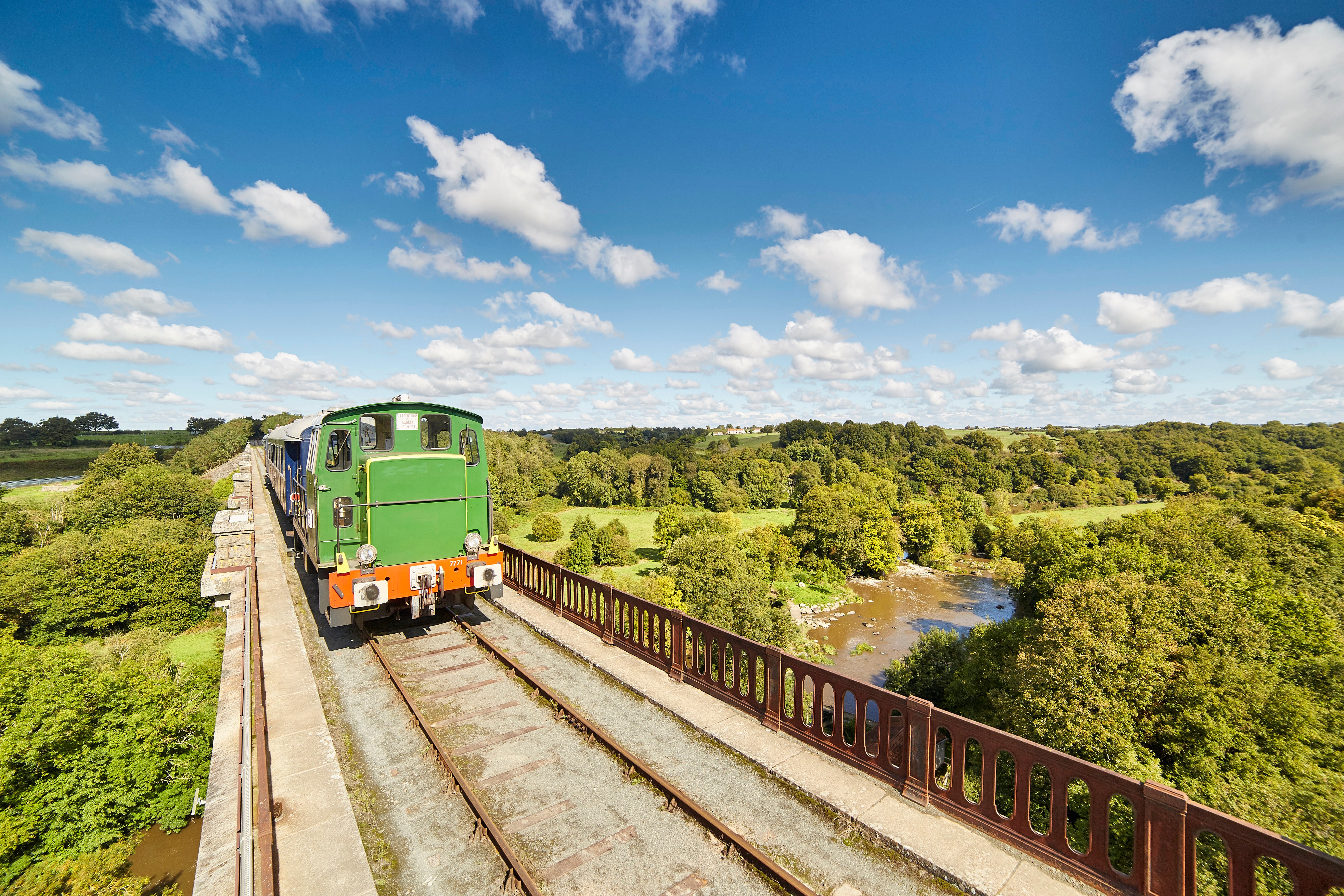 Train de la Vendée passant sur un pont au dessus d’une rivière dans une campagne  verdoyante