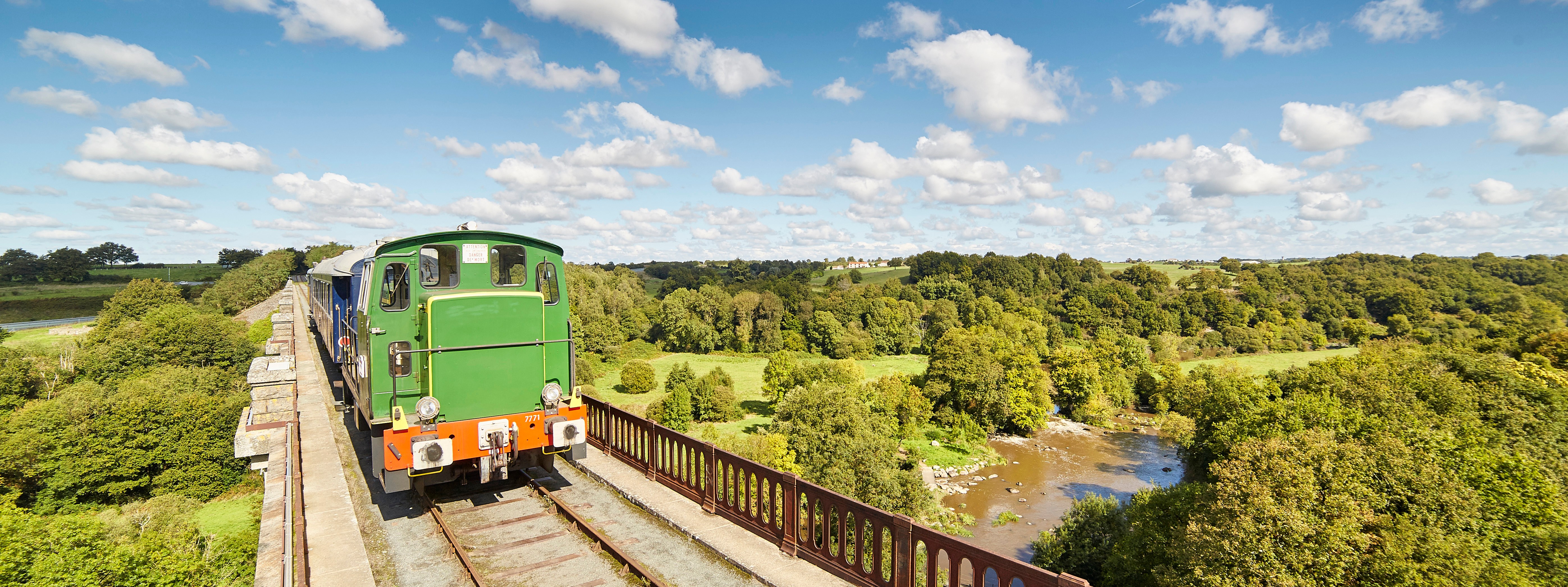 Train de la Vendée passant sur un pont au dessus d’une rivière dans une campagne  verdoyante