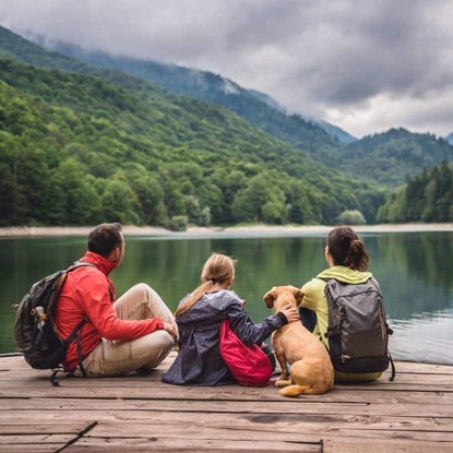 Famille assise sur un ponton en bois près d'un lac entouré de montagnes verdoyantes