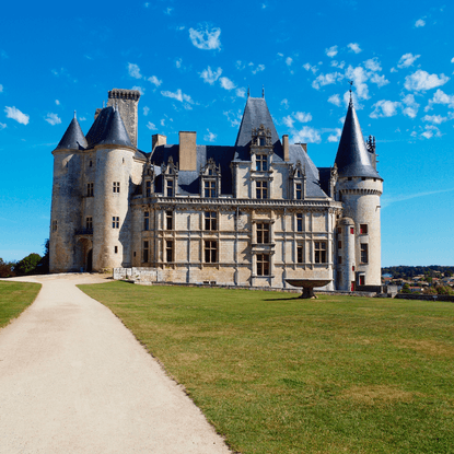 Depuis un chemin à côté d’un jardin d’herbe vert, vue sur l’aile sud du Château de la Rochefoucauld avec sa fontaine sous un ciel bleu.