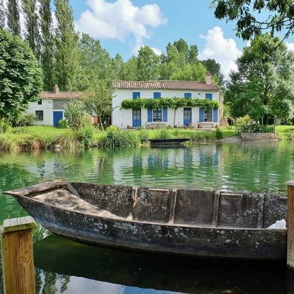 Barque amarrée sur le marais aussi appelé Venise Verte devant une maison maraîchine entourée de verdure.