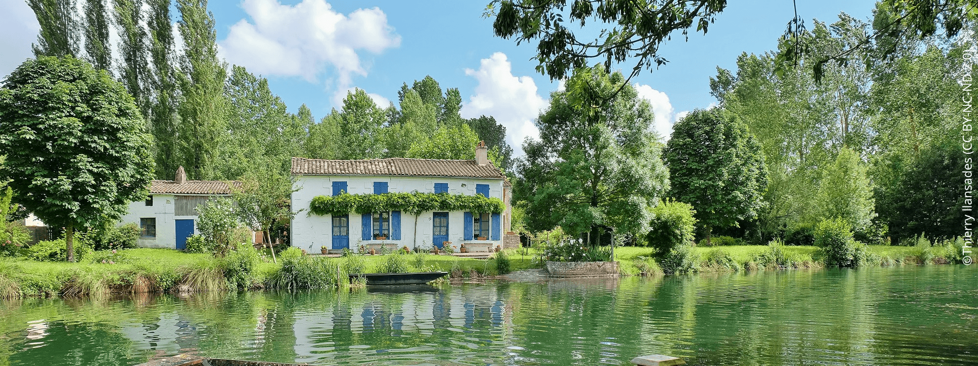 Barque amarrée sur le marais aussi appelé Venise Verte devant une maison maraîchine entourée de verdure.