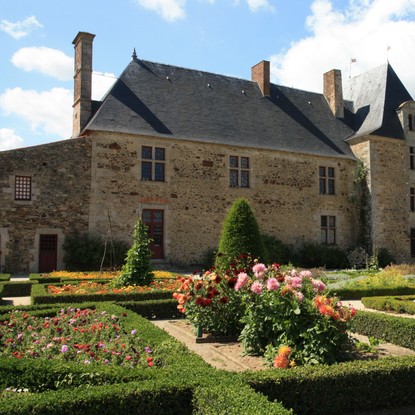Jardin à la française composé d’arbustes taillés soigneusement et de fleurs qui devancent la partie château du Logis de la Chabotterie.