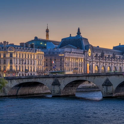 Vue sur un pont de Paris avec le musée d'Orsay en arrière-plan au coucher du soleil, sous un ciel dégagé.