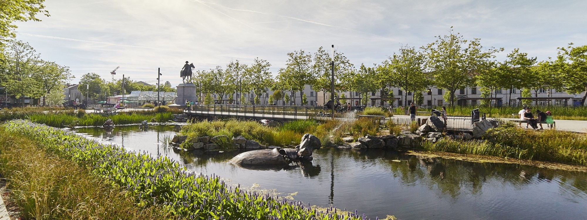 Vue sur les bassins entourés de verdure et les animaux mécaniques de la place Napoléon