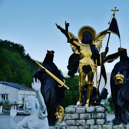 Location de vacances à Domrémy la Pucelle : Statue de Jeanne d’arc écoutant ses voix à côté de son père et de sa mère en couleur blanche, noir et or. / Licences Creative Commons