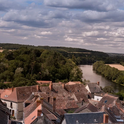 Vue des toits des maisons en hauteur de La Roche Posay, au loin la rivière et bordés d’arbres
et de champs sur un fond nuageux d’été