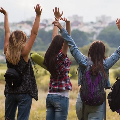 Groupe de jeunes levant les bras dans un paysage naturel, avec une ville en arrière-plan.