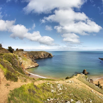Vue panoramique sur la mer et plus précisément sur une petite crique paradisiaque avec une côte rocheuse sous ciel bleu avec quelques nuages.