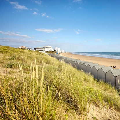 Depuis les dunes sauvages, vue sur la grande plage de Saint Gilles Croix de vie avec les cabanes de plage sous un beau ciel bleu