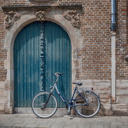 Un vélo garé devant une porte ancienne en bois bleu, entourée de briques.