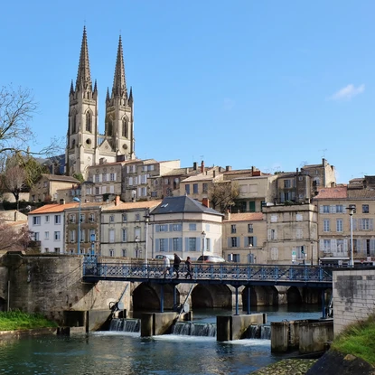 Pont traversant la Sèvre Niortaise menant à des habitations surélevées et l’église Saint André de Niort qui trône derrière.