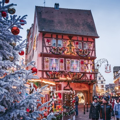 Maison alsacienne ornée de décorations de Noël à Colmar avec un grand sapin enneigé.