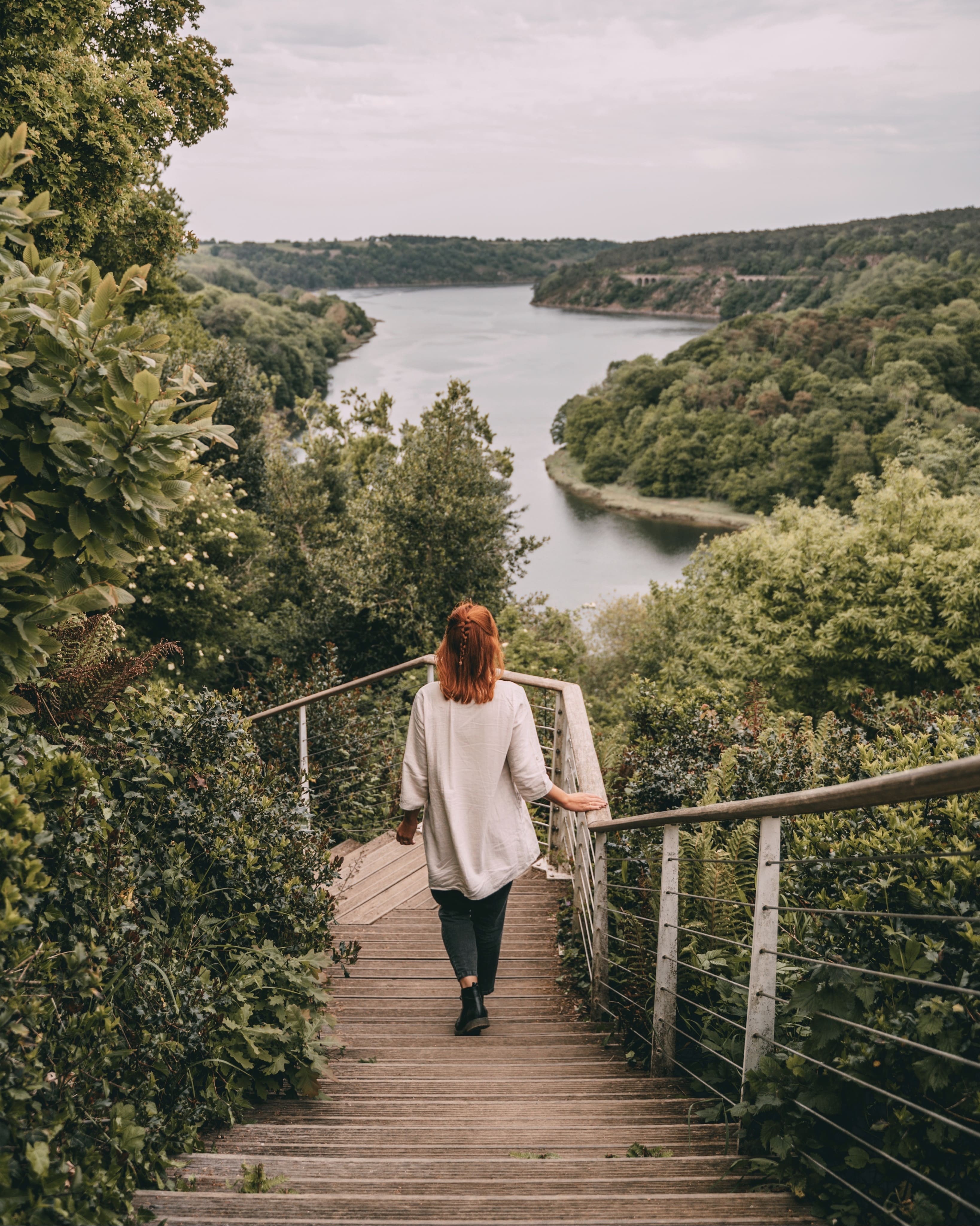  Femme rousse descendant vers la rivière du Trieux depuis le château de la Roche-Jagu sur un escalier de bois avec un ciel nuageux