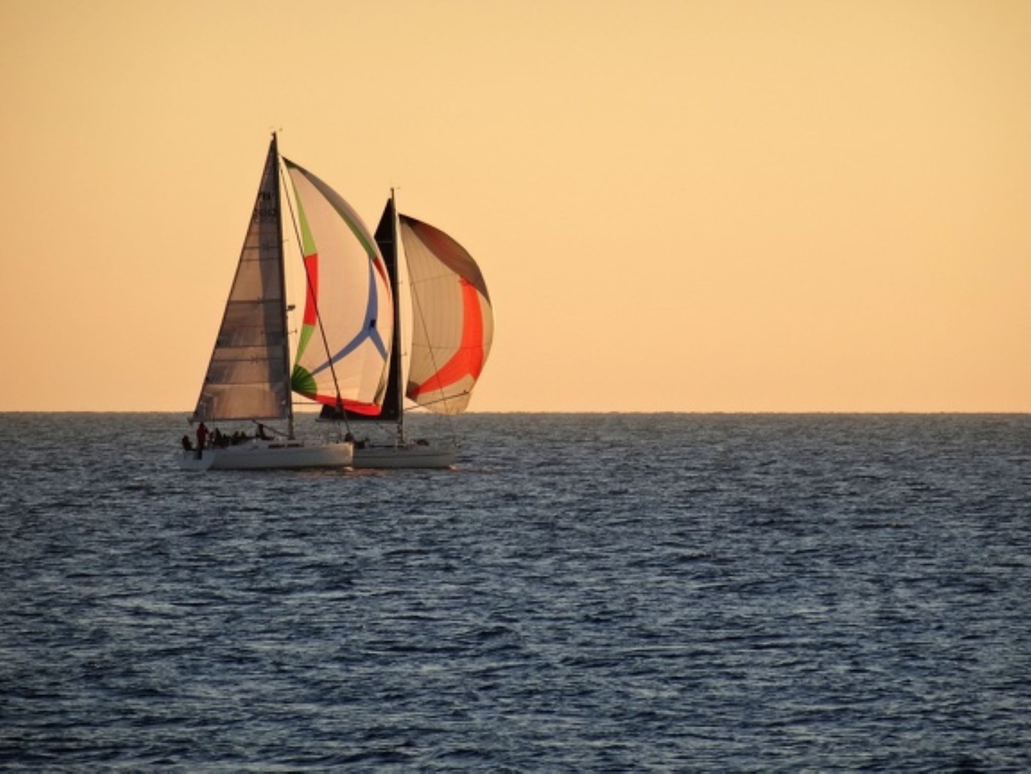 Deux voiliers avec des voiles colorées naviguant sur la mer au coucher du soleil 