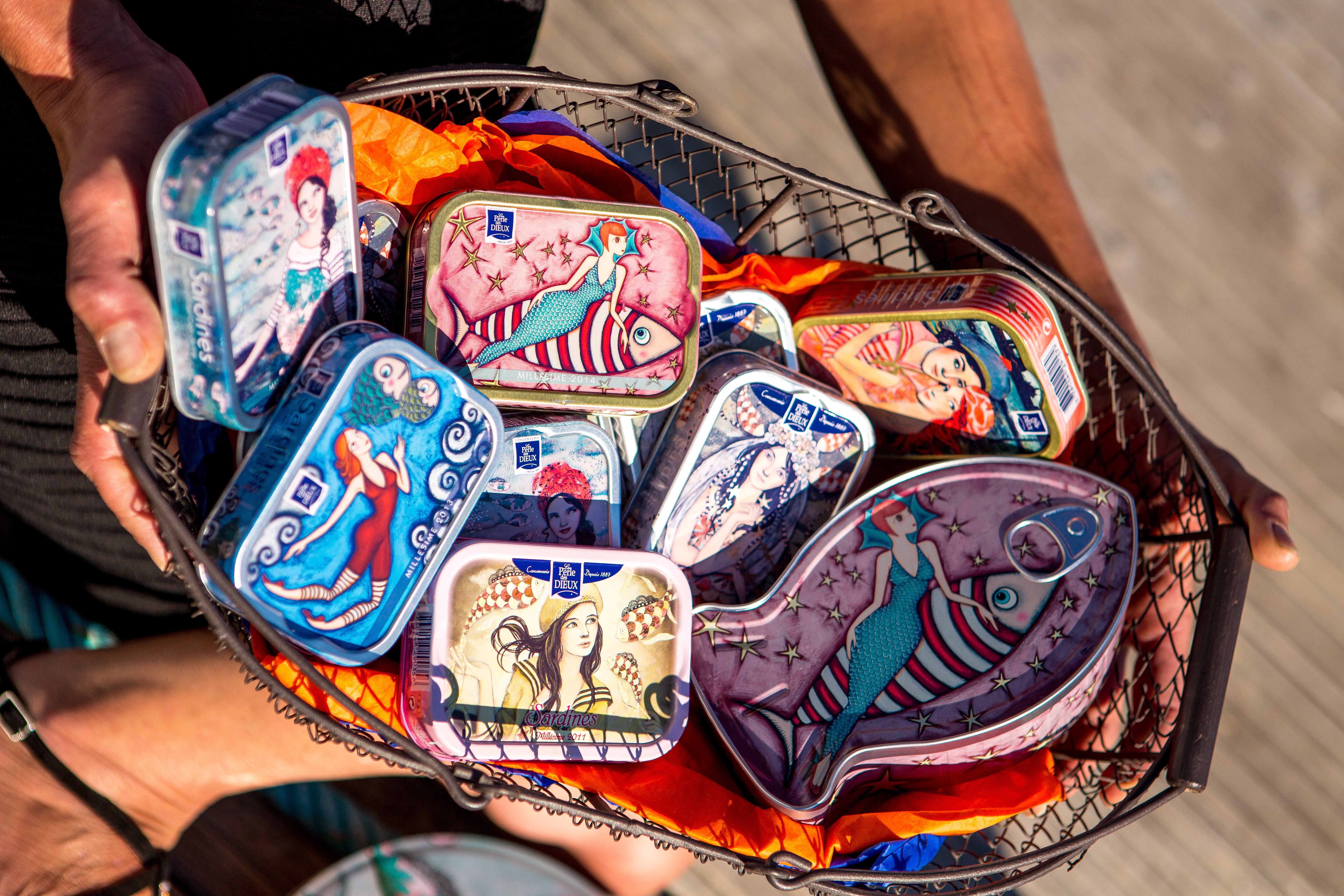 Dans un panier en métal, conserves colorées de Sardines, poisson incontournable pêché à Saint Gilles Croix de Vie