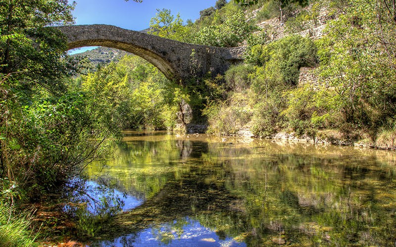 Pont en pierre au-dessus d’une rivière entourée de végétation luxuriante au Cirque de Navacelles sur le chemin de Compostelle