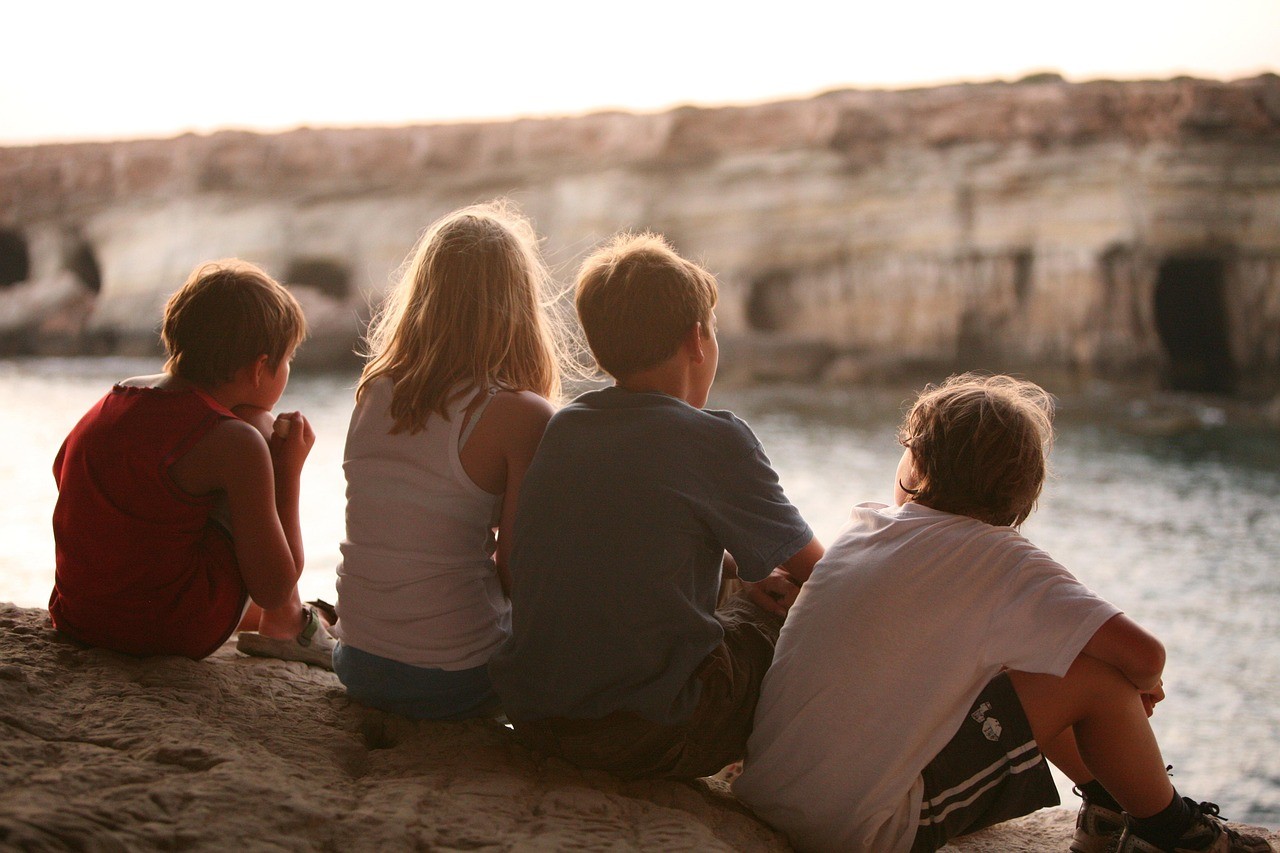 Quatre enfants assis face à la mer, admirant le paysage au coucher du soleil.