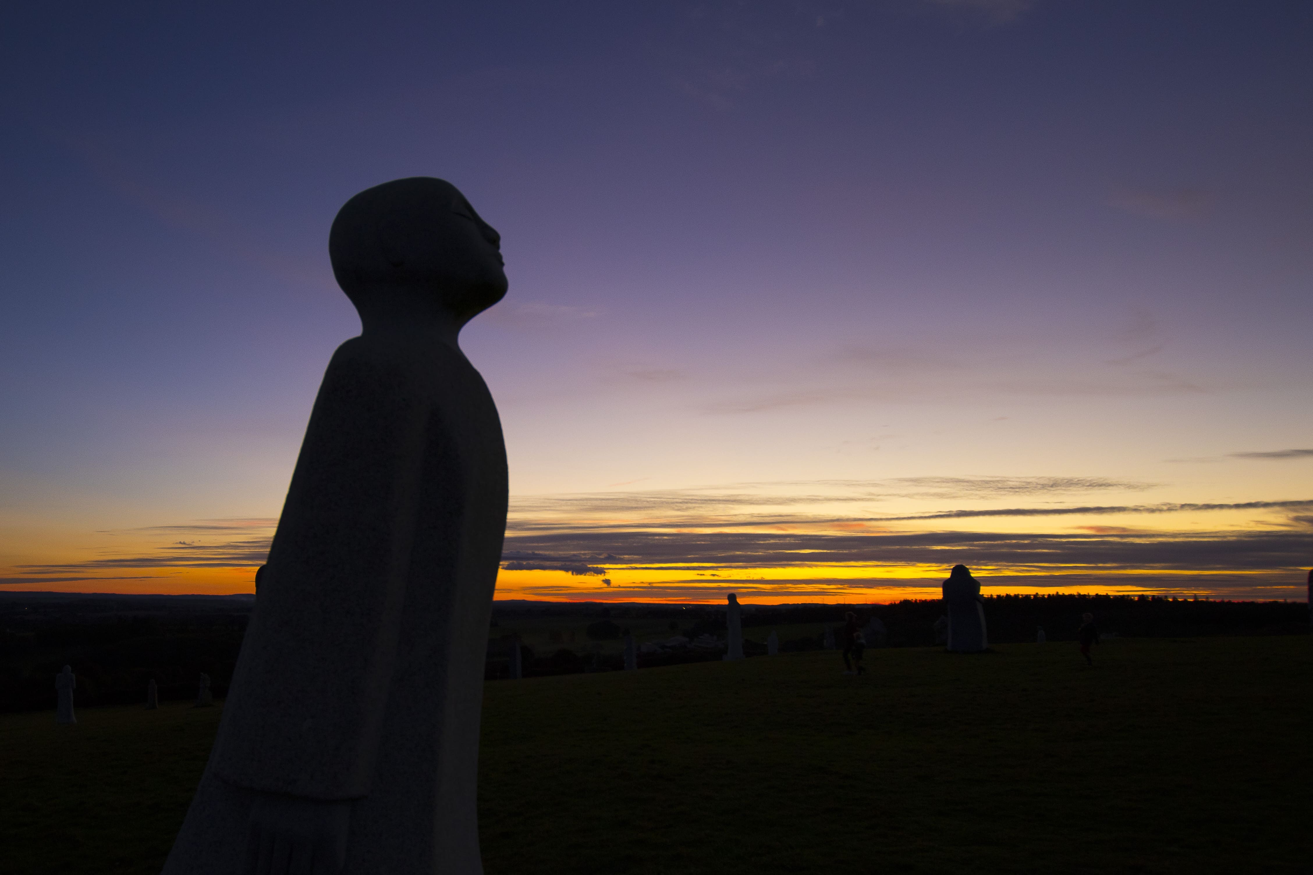 Vue de profil d’une statue de la Vallée des Saints à Carnoët par coucher de soleil avec lumière rose orangée