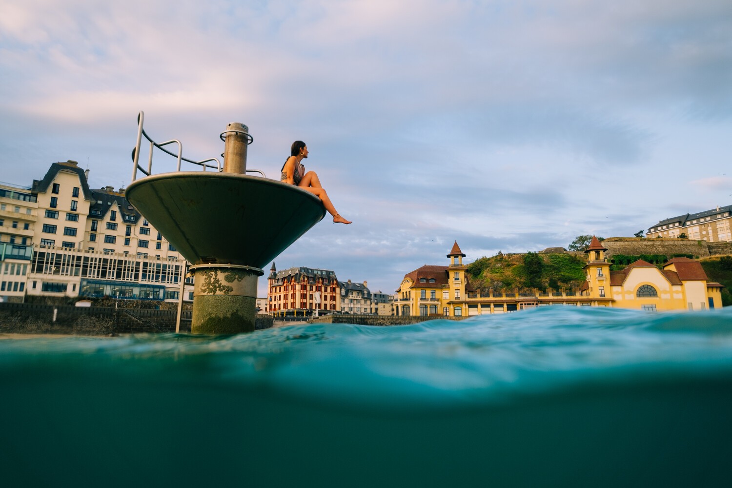 Baignade d'une femme dans l'eau bleue de la Manche, sur la plateforme de la plage. En arrière plan, le casino de Granville et les maisons typique normandes, ciel légèrement nuageux et lumières de fin de journée