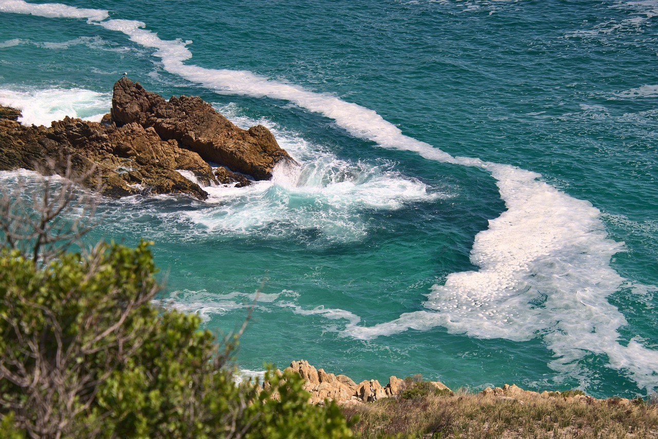 Rochers entourés d'une eau turquoise et des vagues blanches sur un littoral sauvage.