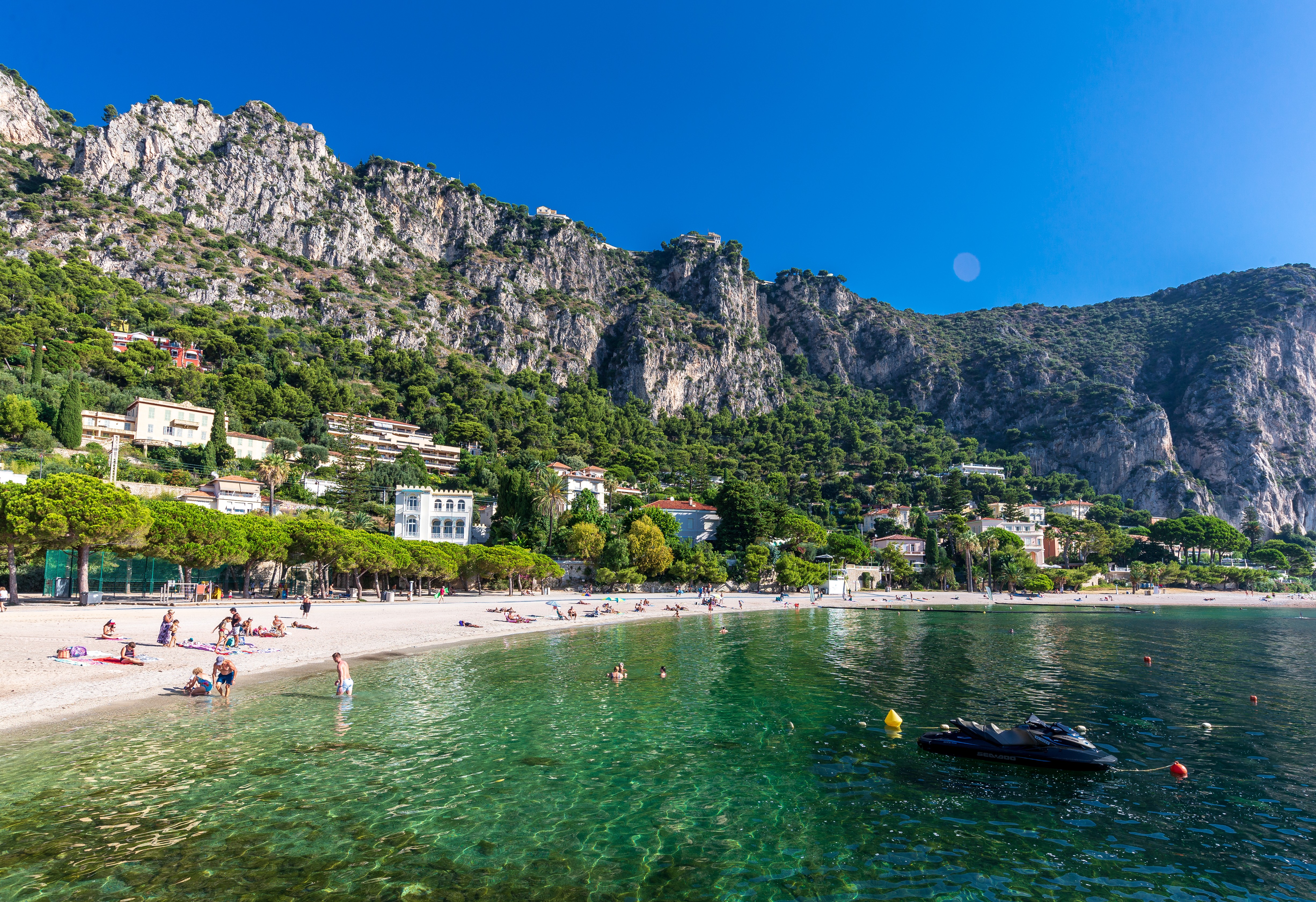 Plage de sable fin à Beaulieu-sur-Mer sur la Côte d’Azur avec ses eaux cristallines et la côte rocheuse en arrière-plan sous un ciel bleu