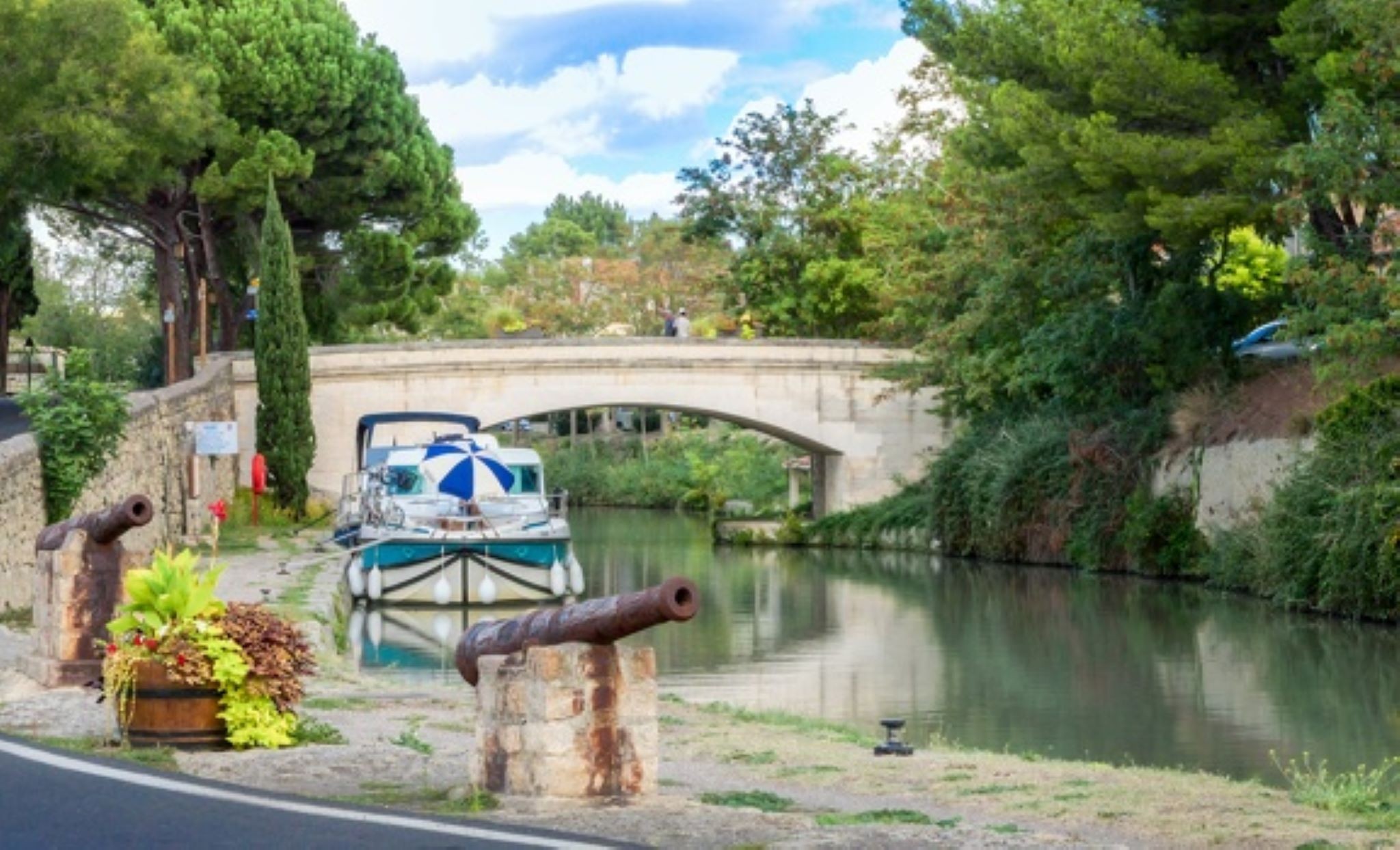 Bateaux amarrés le long du canal de midi avec un pont en pierre en arrière-plan et des arbres verdoyants 