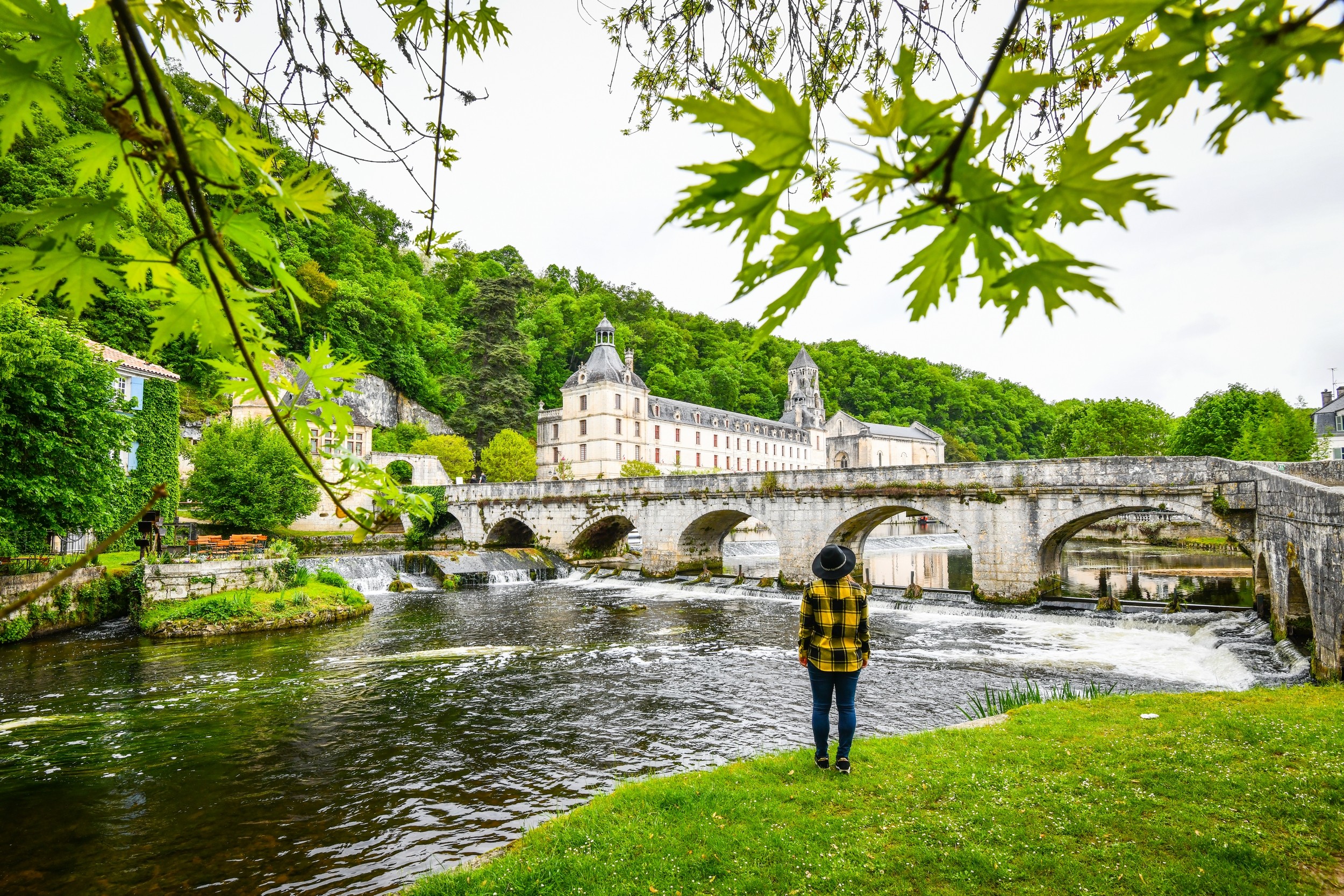 Une femme debout devant une rivière avec un pont en arrière-plan.