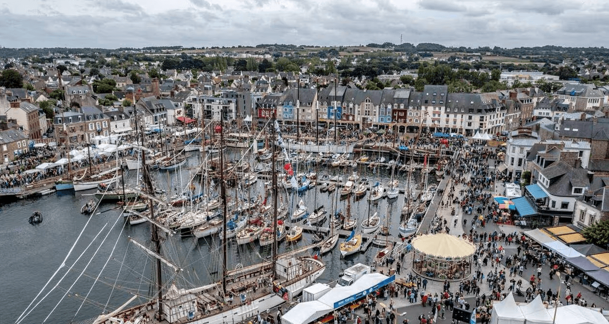 Vue aérienne du port de Paimpol pendant le Festival du Chant de Marin, avec des bateaux traditionnels et une foule animée.