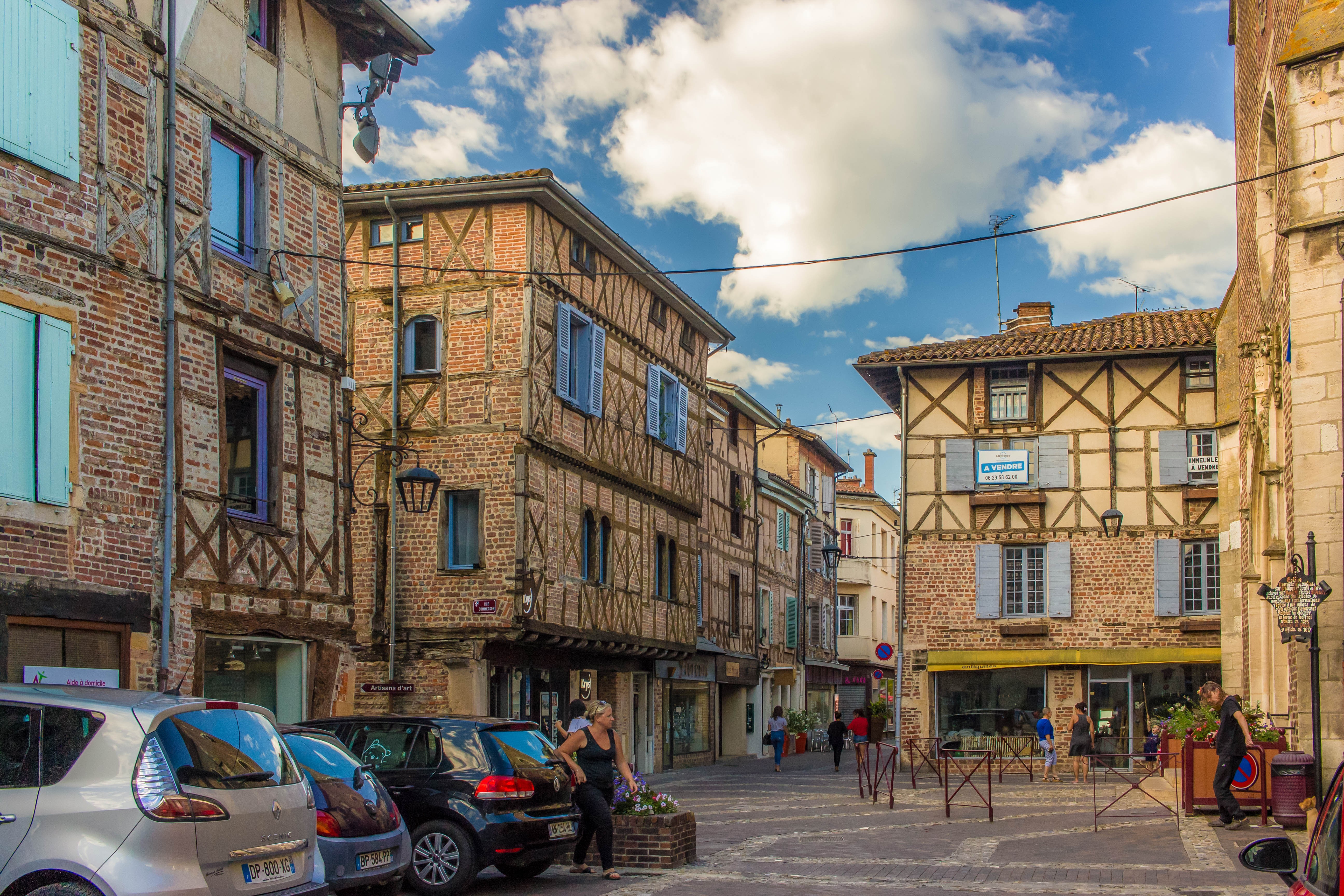 Rue commerçante de Châtillon-sur-Chalaronne sous un ciel bleu avec quelques nuages, avec une architecture médiévale, petite brique et poutre apparente