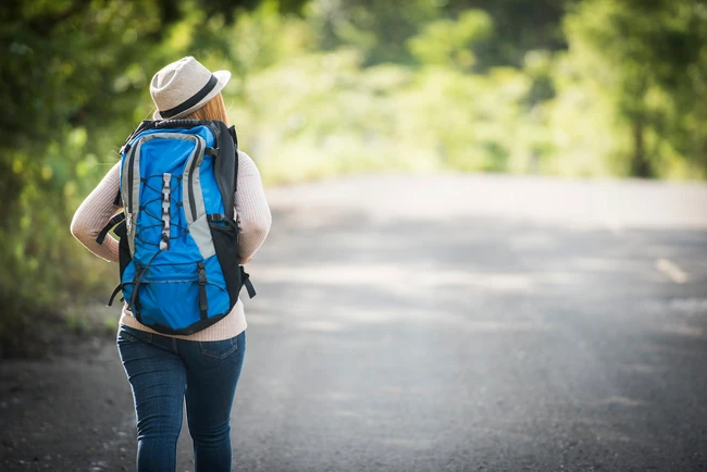Randonneuse avec un sac à dos bleu, marchant sur une route entourée de verdure.
