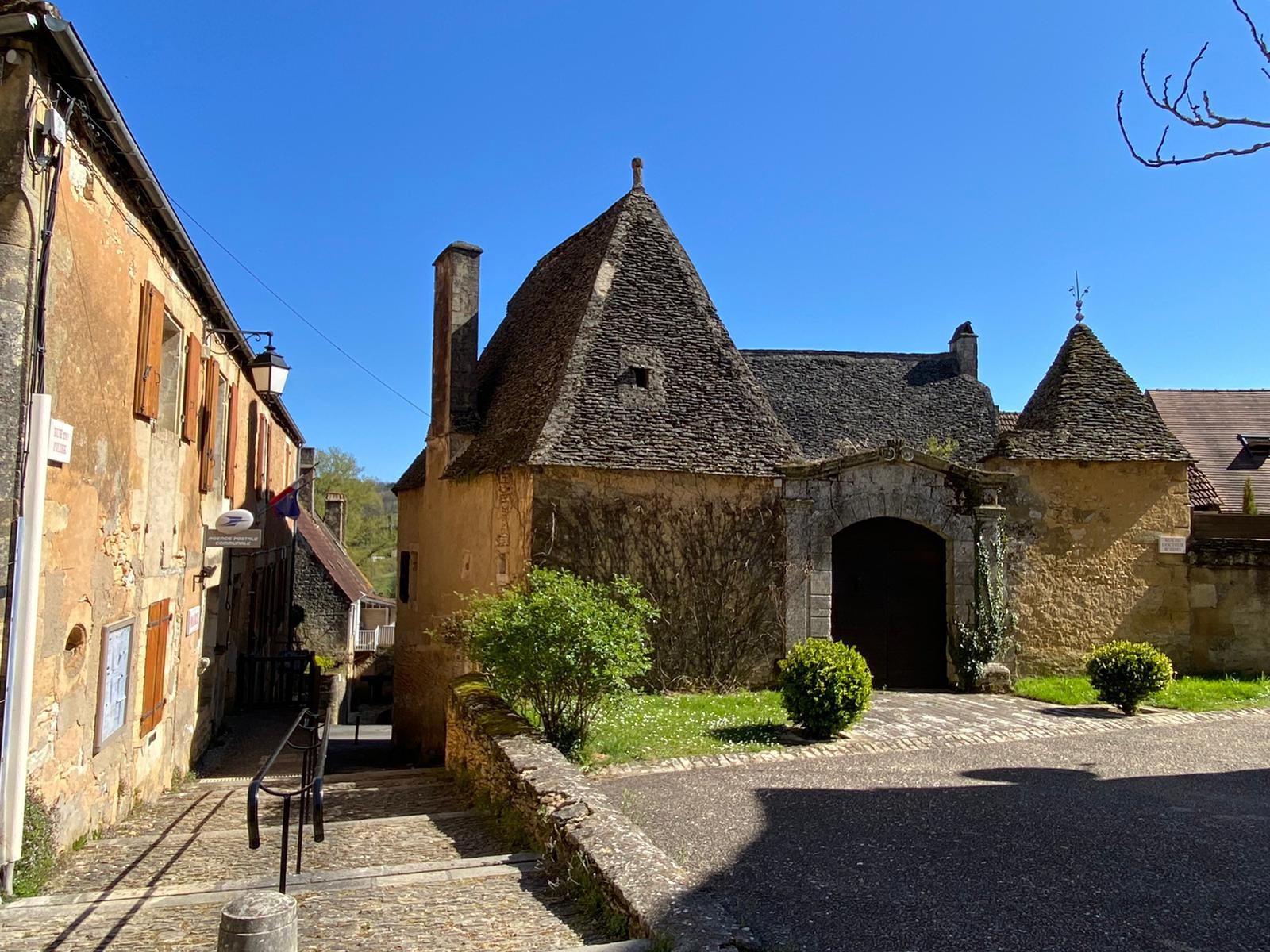 Vieille bâtisse en pierre avec toitures en lauze à Meyrals, Dordogne, représentant l’architecture traditionnelle du Périgord Noir sous un ciel bleu clair.