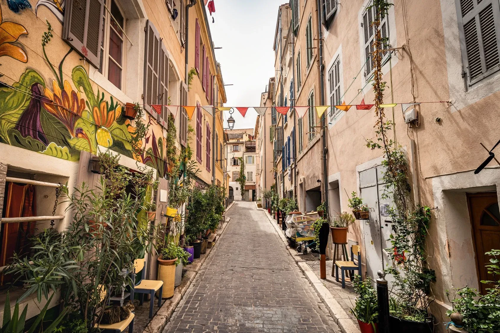 Rue étroite et colorée à Marseille, ornée de plantes en pots et de guirlandes décoratives entre les bâtiments.