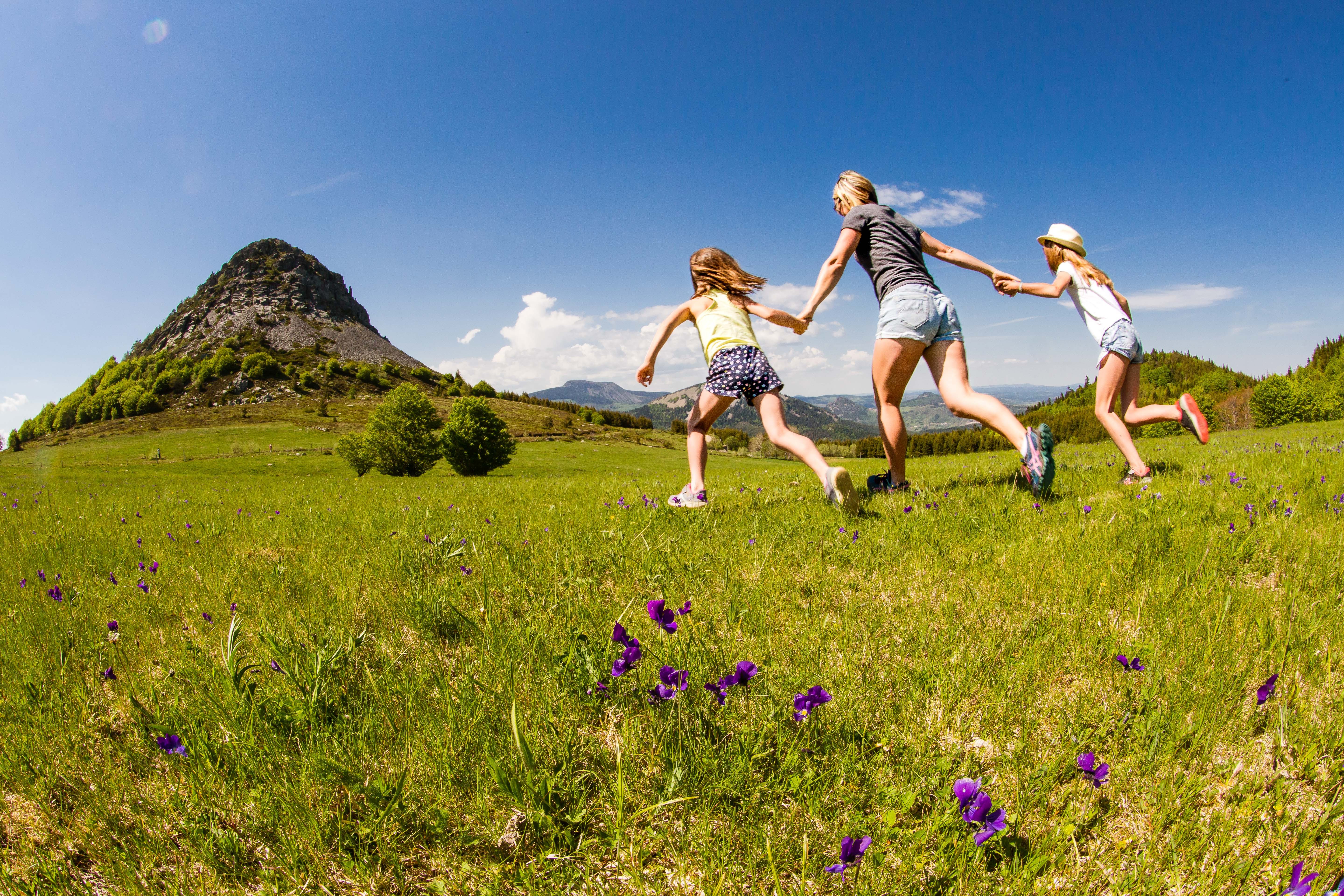 Famille qui joue dans les champs au pied du Mont Gerbier de Jonc sous un beau ciel bleu