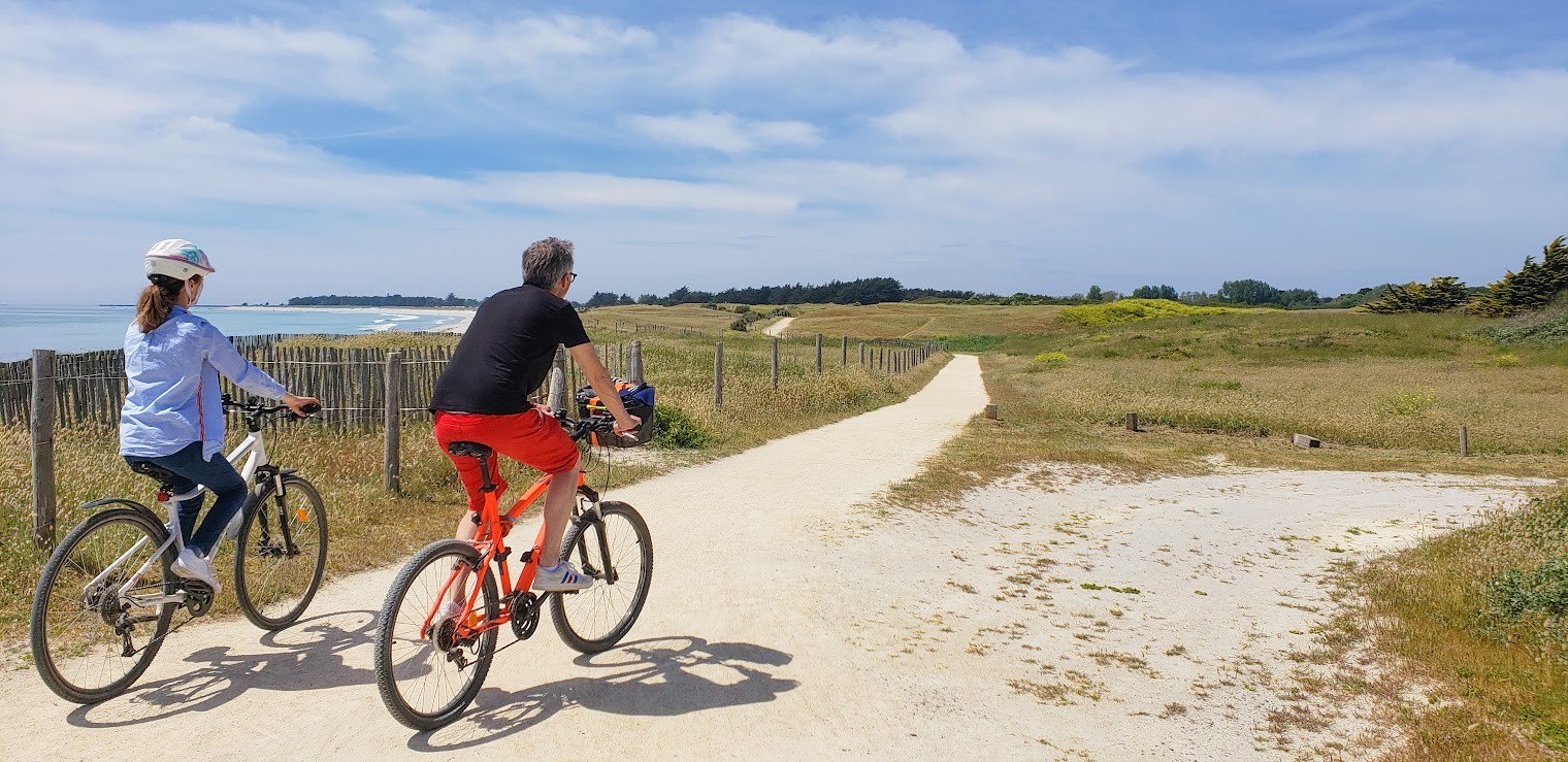 Balade en couple à vélo sur le sentier des dunes en bord de mer par beau temps