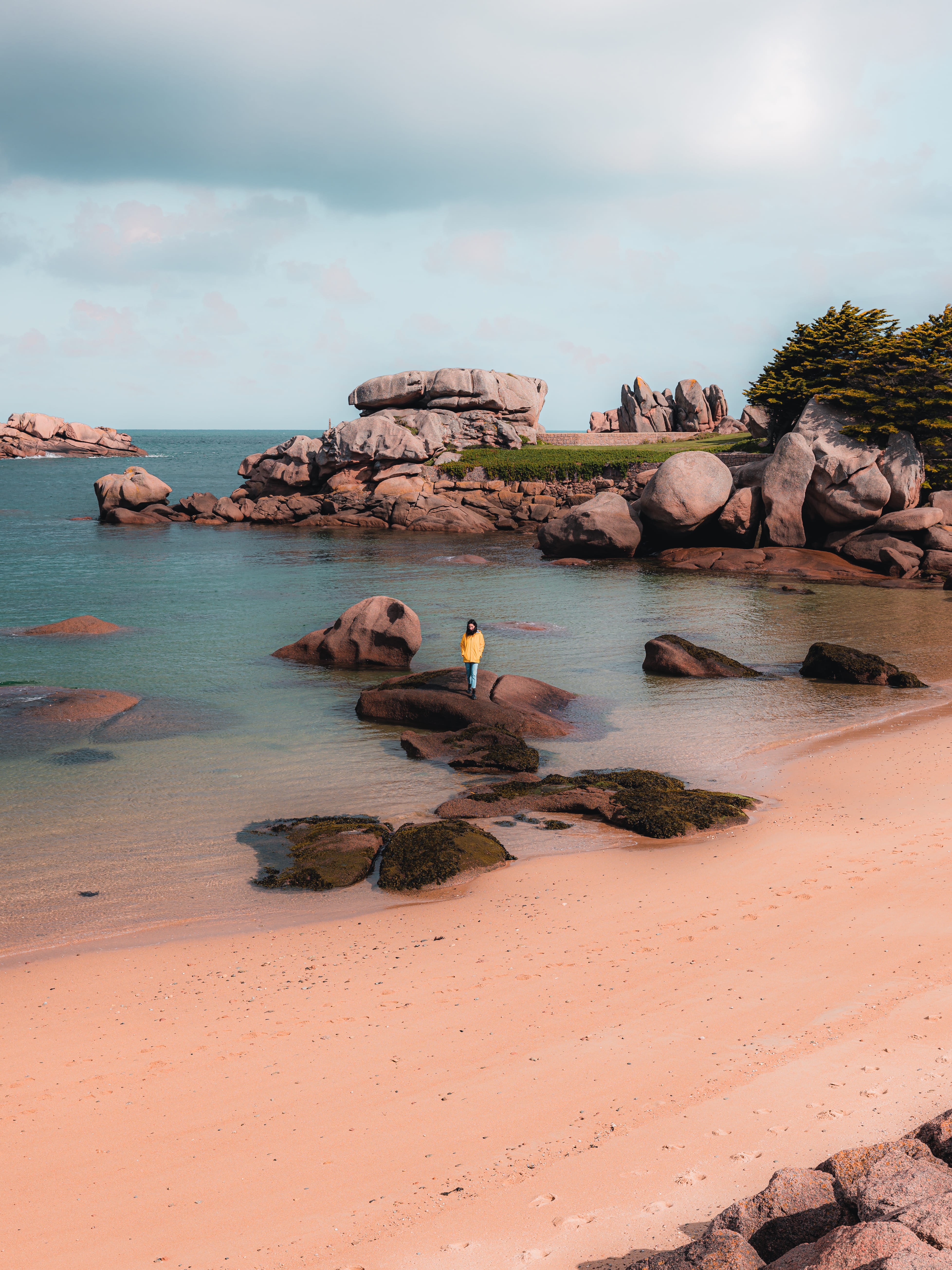  Jeune femme ciré jaune marchant de rocher en rocher à Tregastel, île Renote, Côte de Granit Rose