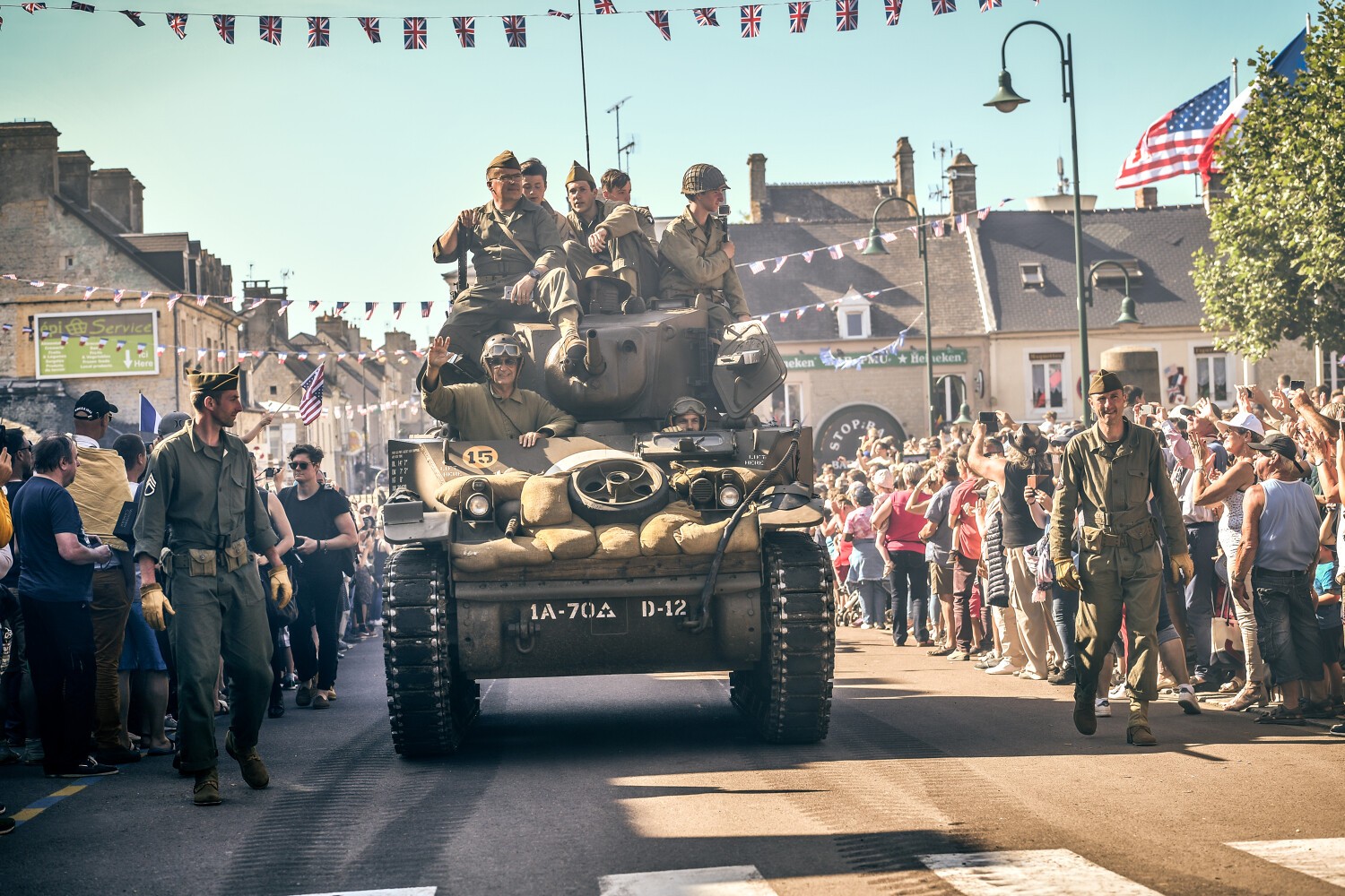 défilé dans les rues du char chargé de soldats saluant la foule, drapeaux anglais, américain et français accrochés dans la rue, foule qui prend des photos