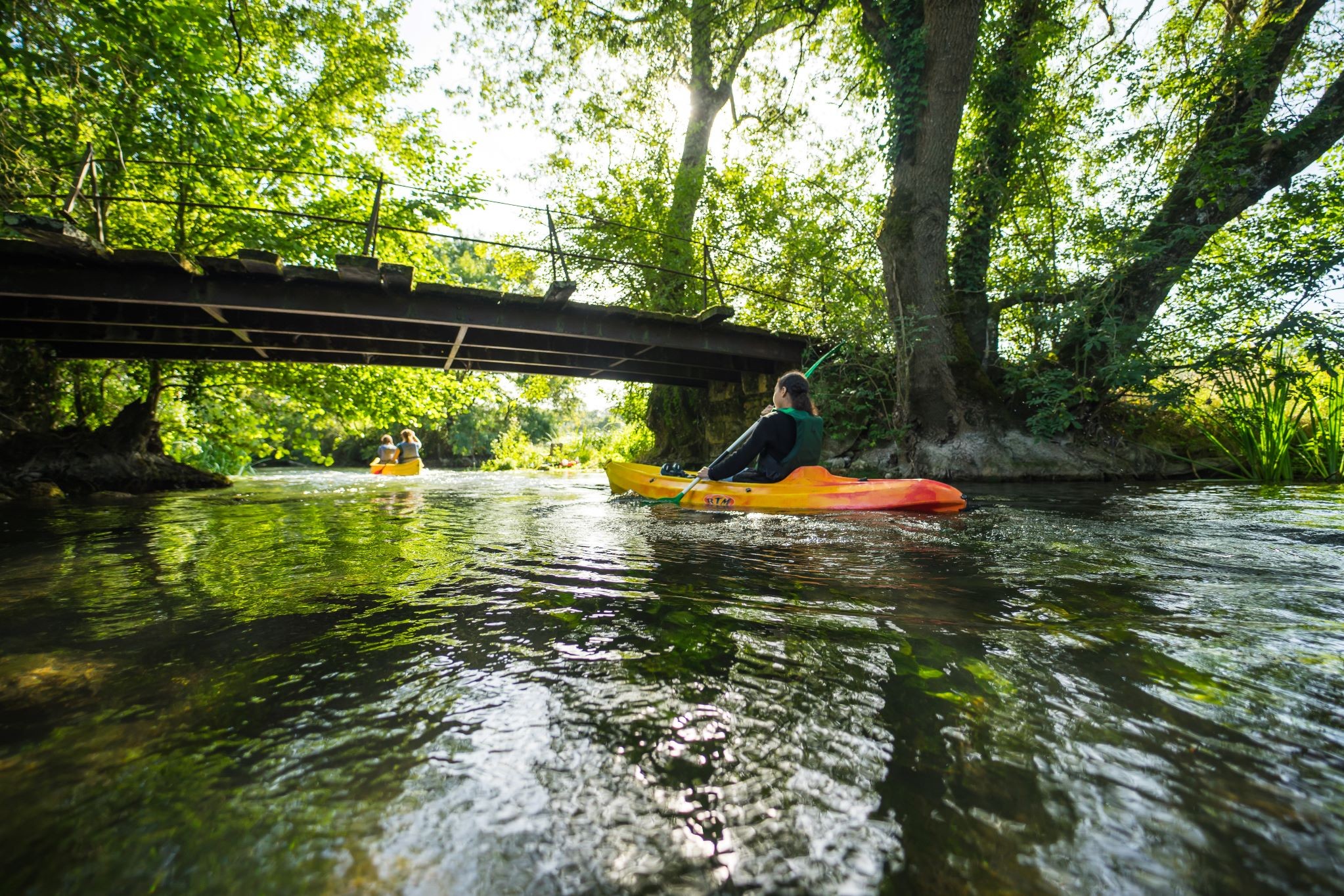 Sur le Clain, deux canoés l’un derrière l’autre passent sous le petit pont en métal