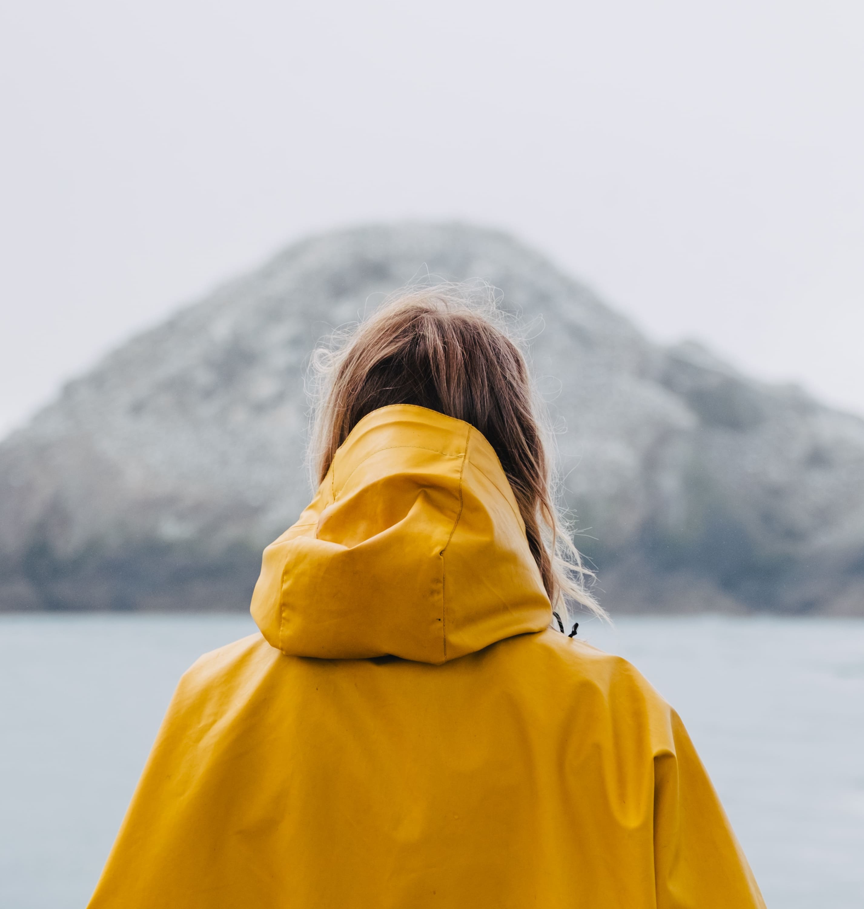Femme avec ciré jaune regardant les Sept îles avec vue mer et ciel couvert  sur la côte de Granit Rose Perros Guirec