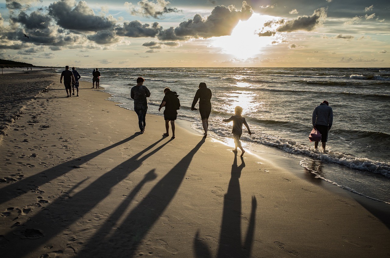 Plage au coucher de soleil avec silhouettes de personnes marchant au bord de l'eau.